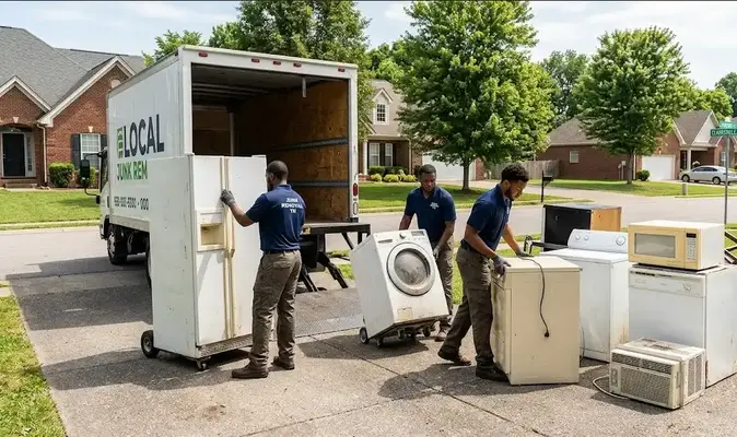Junk removal crew in Clarksville loading old appliances including a refrigerator, washer, dryer, microwave, dishwasher, and air conditioning unit onto a truck for disposal and recycling.