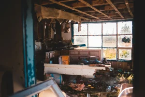 Abandoned room with broken windows, debris, and exposed ceiling beams.